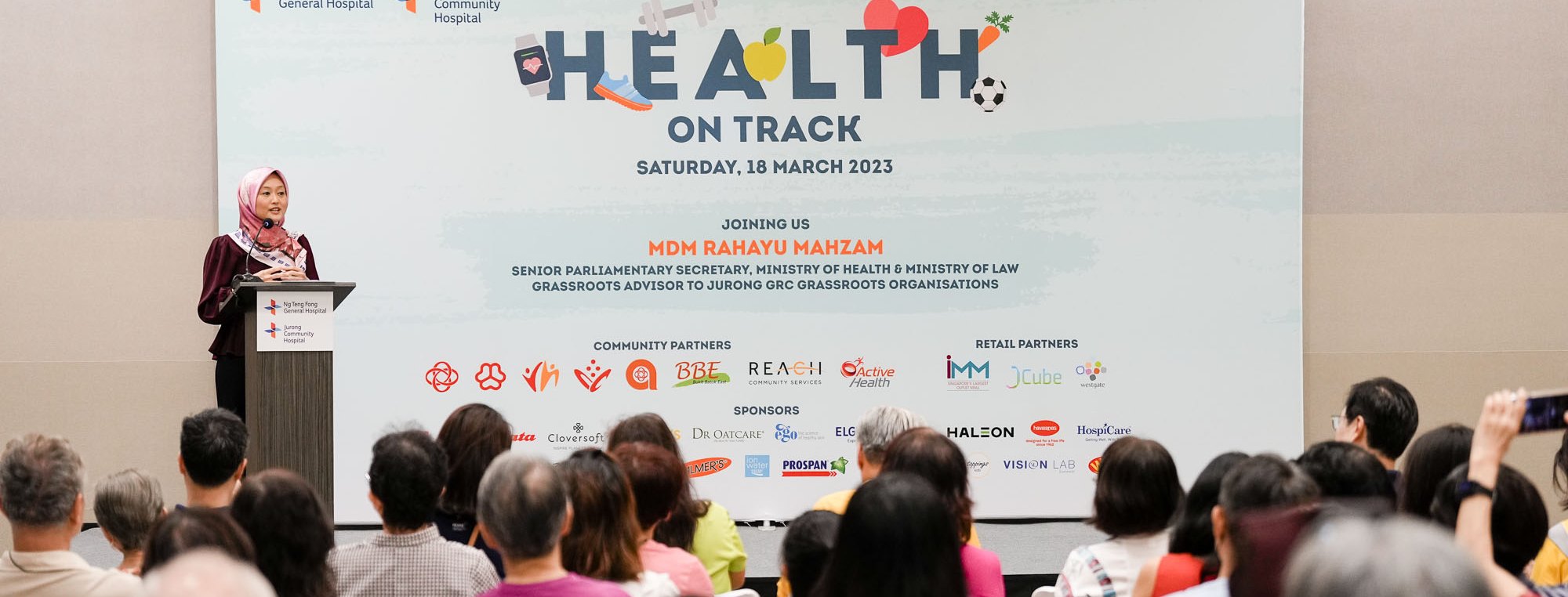 A speaker opening a community health festival from the podium, in front of a seated audience