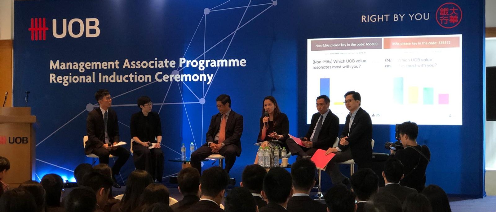A panel on stage at an induction ceremony, in front of a full audience