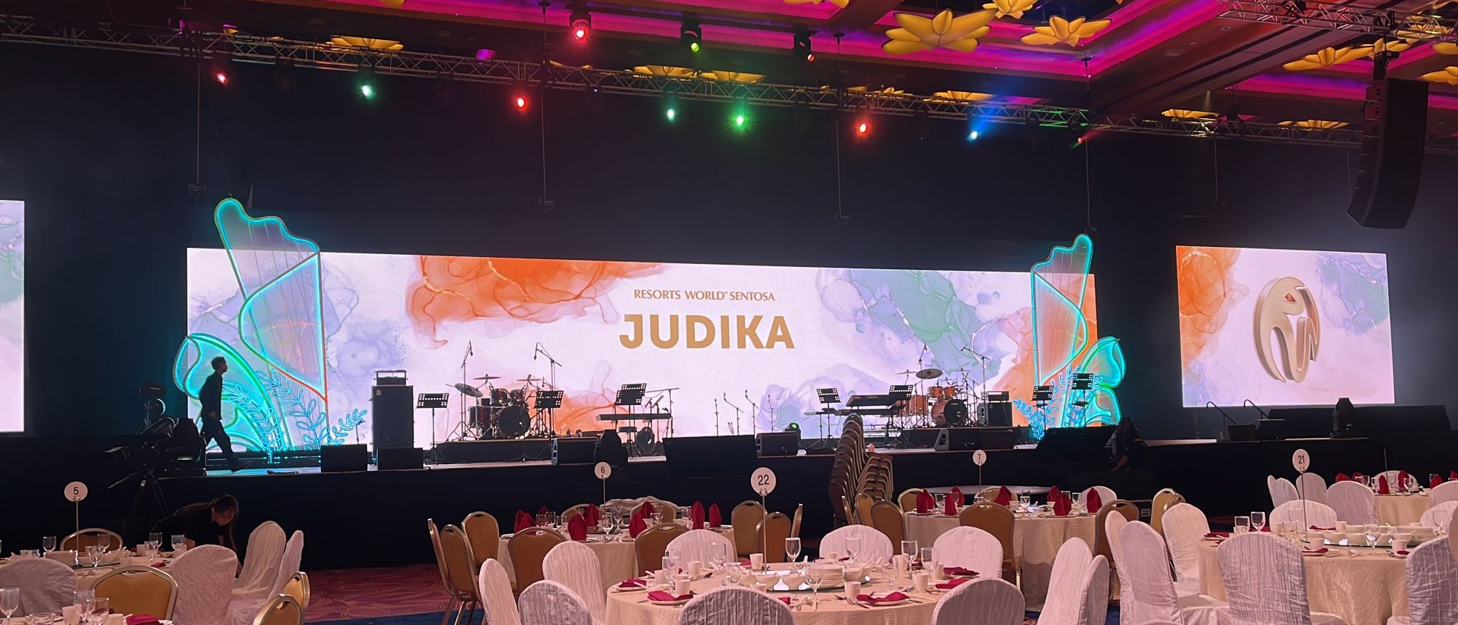 A concert stage at a gala dinner, framed by a wide LED wall with watercolour artwork and the artist's name