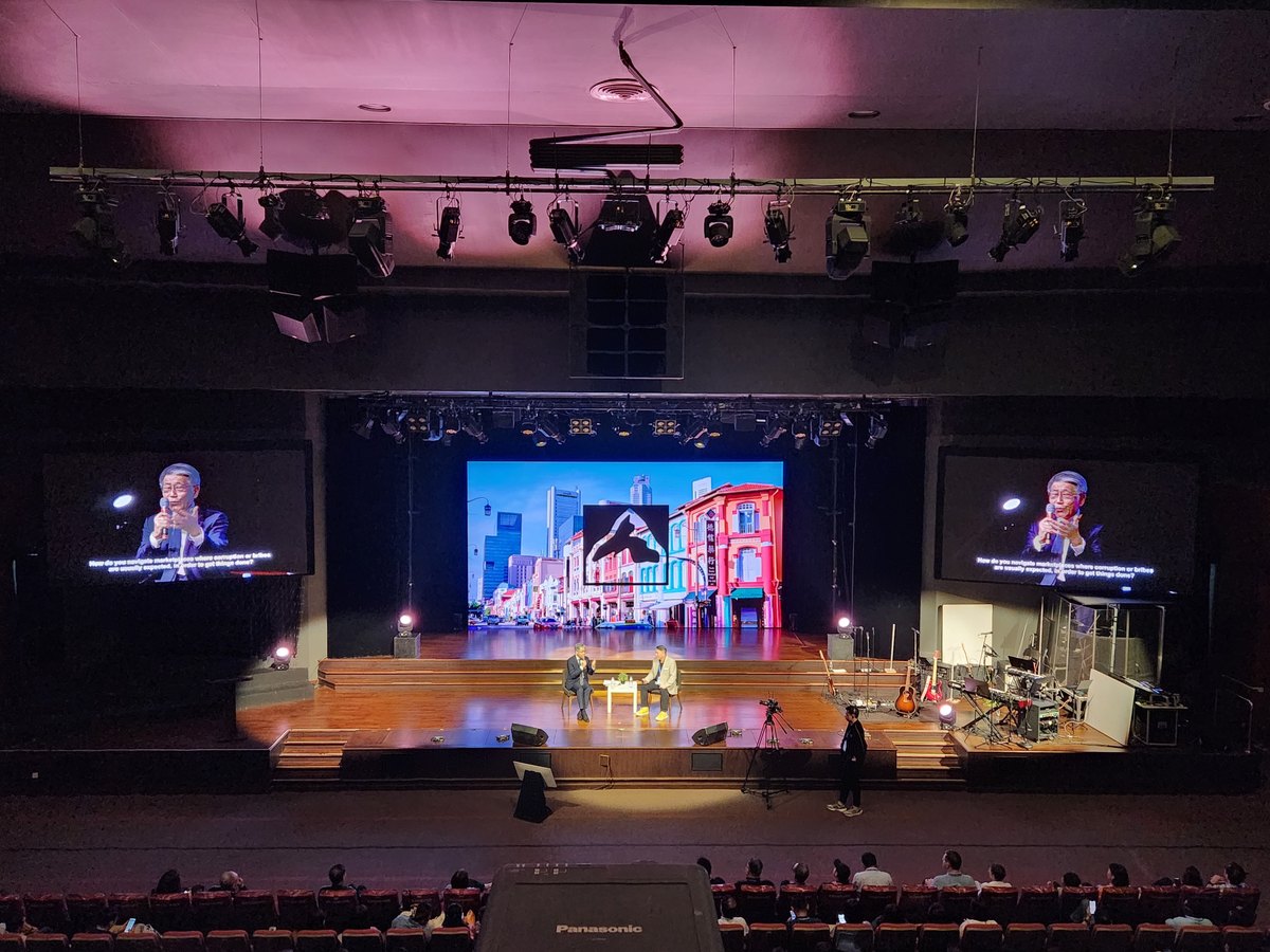 A theatre stage set for a leadership session, with screens on either side