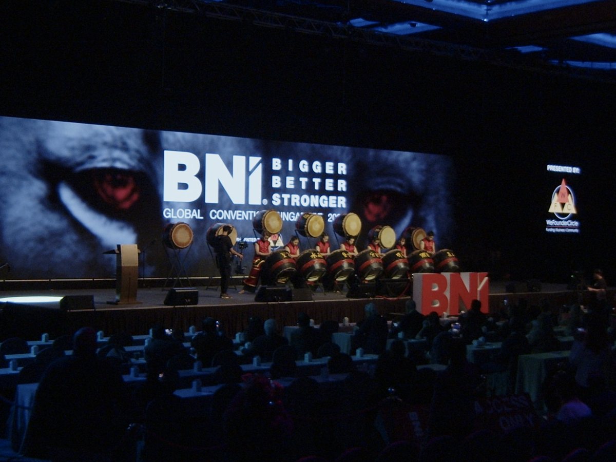 A global convention in session beneath a wide LED screen