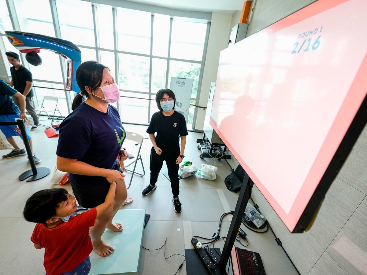 A parent and child playing HDB Runner on the step pad, watching their progress on screen