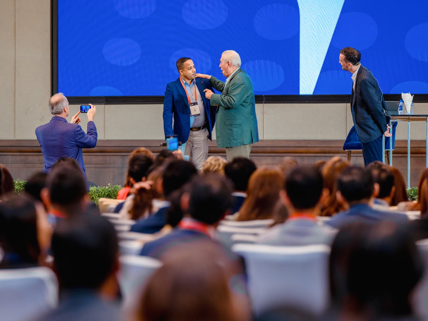 Speakers greeting each other on stage in front of a seated audience