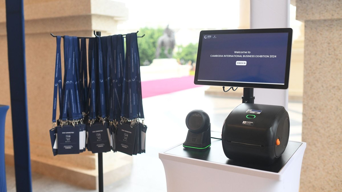 A check-in kiosk with scanner and badge printer, lanyards ready on the rack beside it