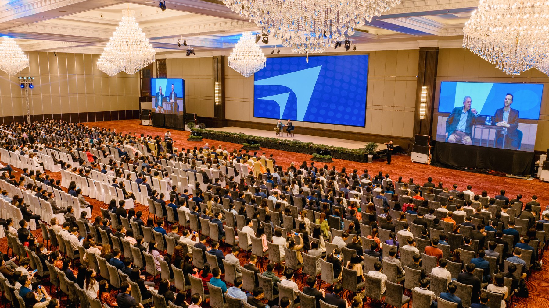 Aerial view of a ballroom plenary, with side screens and a full audience