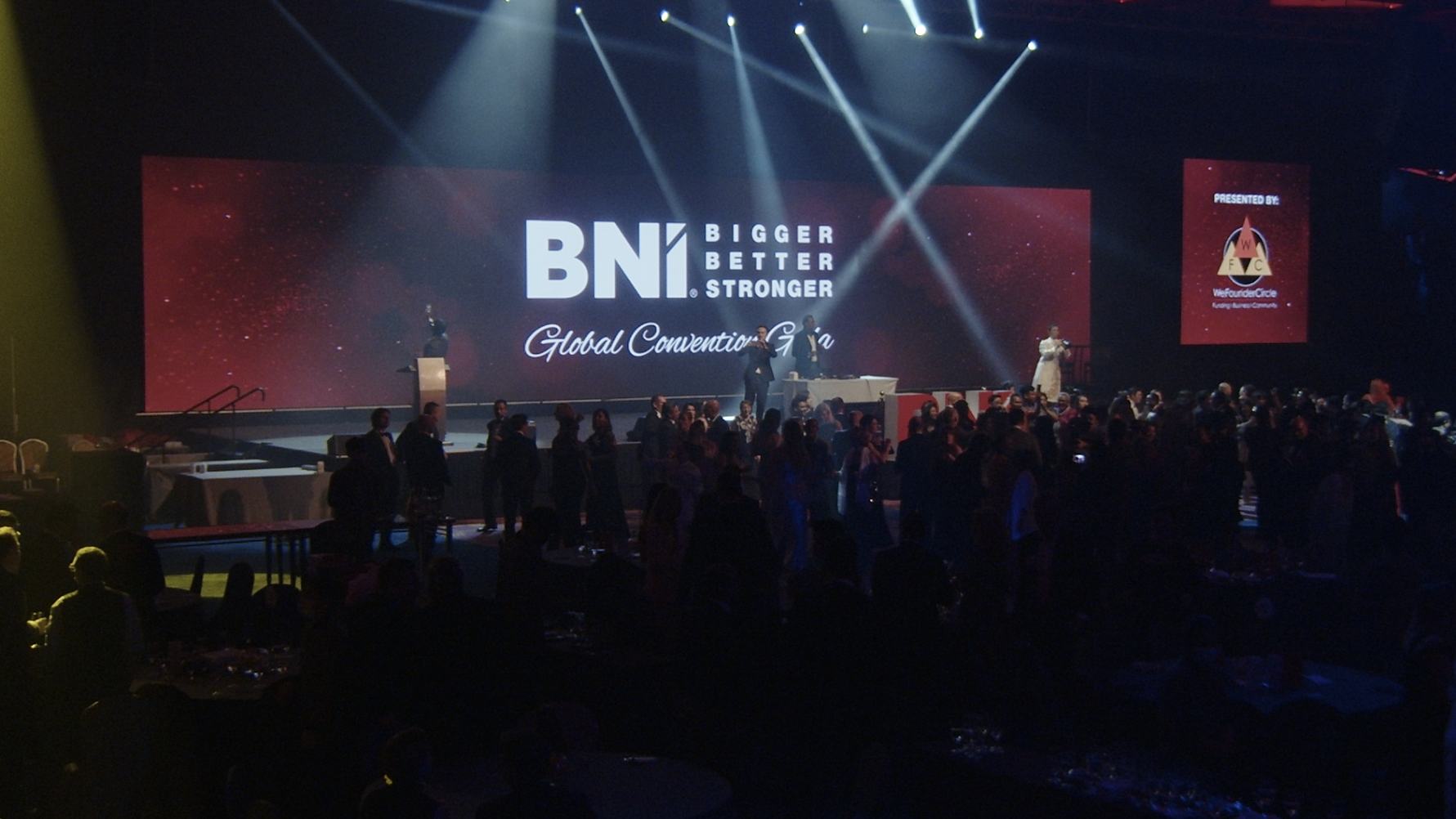 Stage and screens lit for a keynote at a large business convention