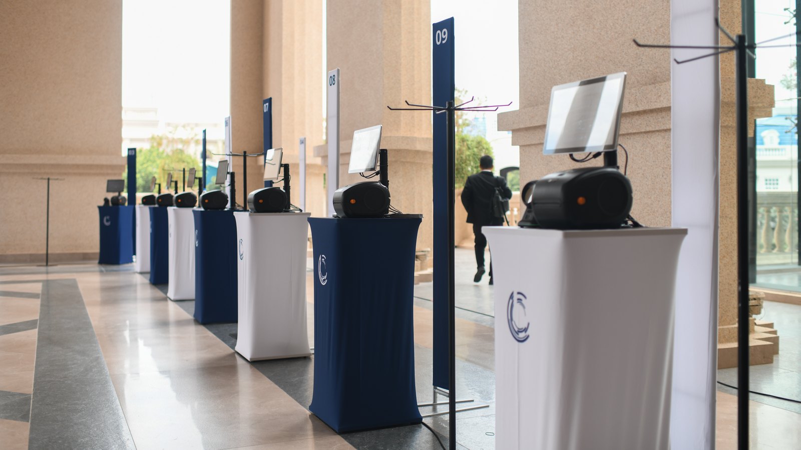 A row of self-service check-in kiosks along a sunlit colonnade