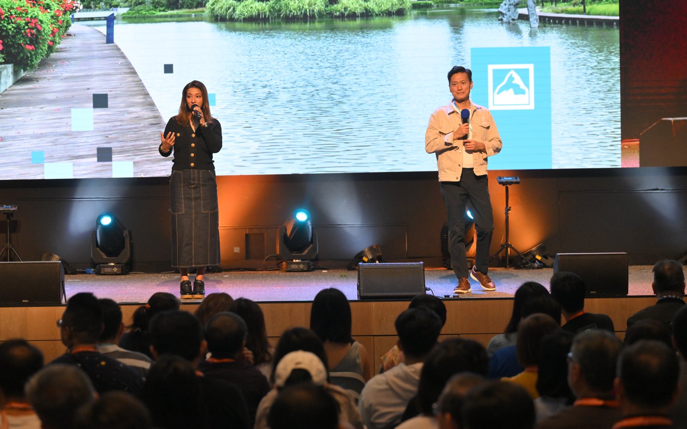 Two speakers presenting on a stage with a large LED backdrop